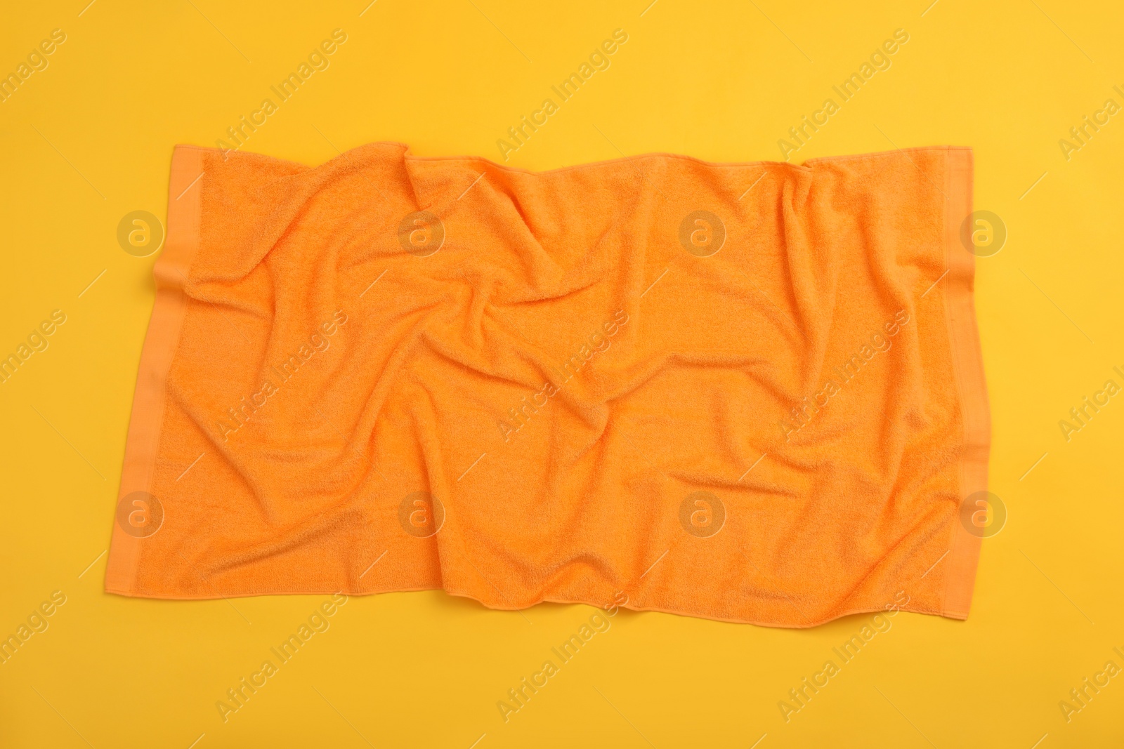 Photo of Crumpled orange beach towel on yellow background, top view
