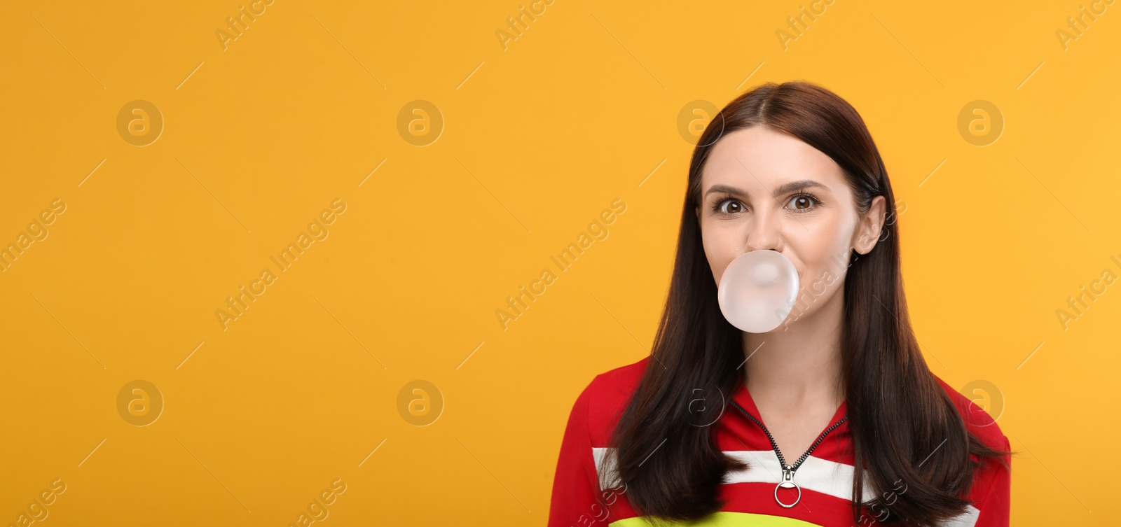 Photo of Beautiful woman blowing bubble gum on orange background, space for text