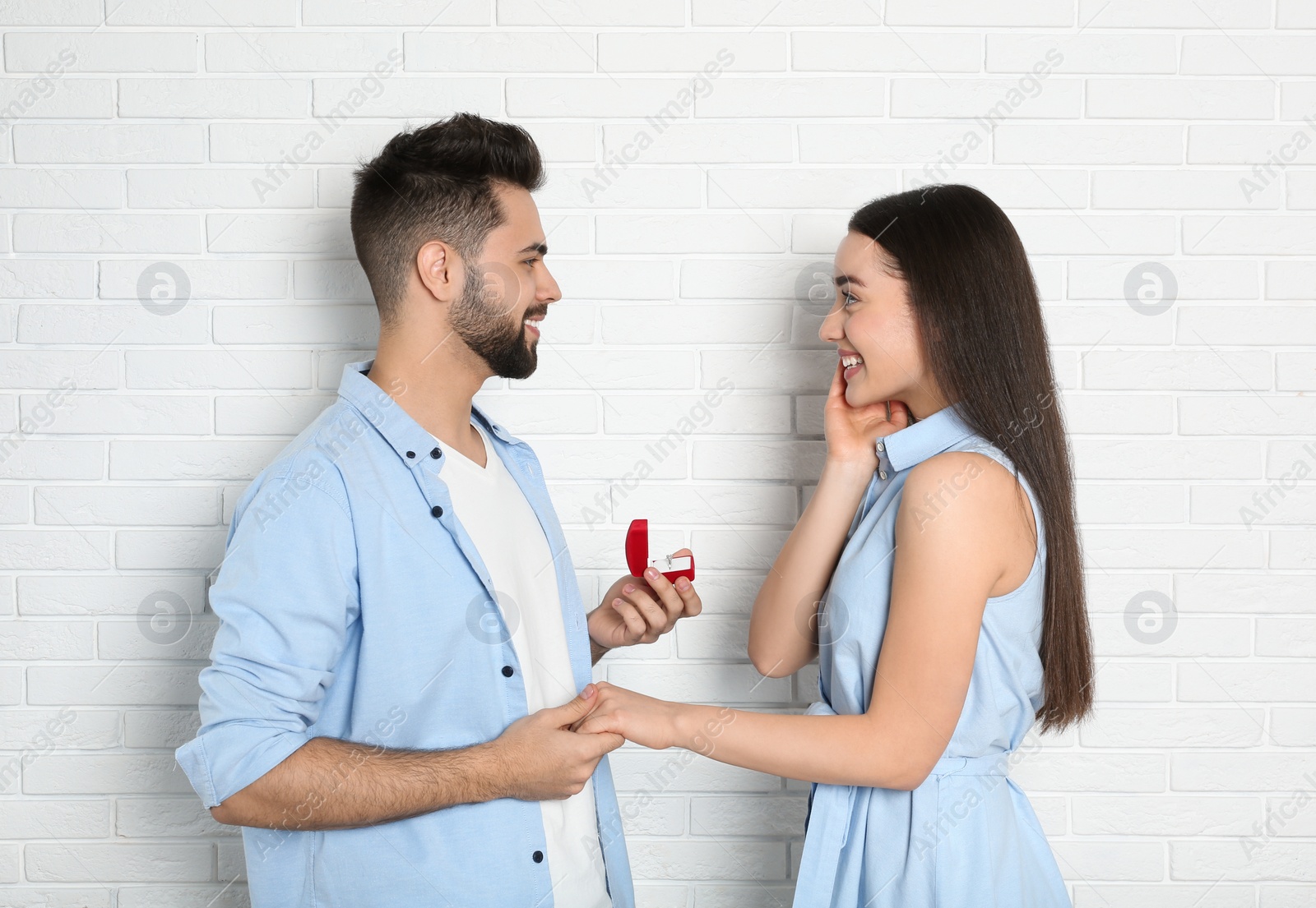 Photo of Man with engagement ring making marriage proposal to girlfriend near white brick wall