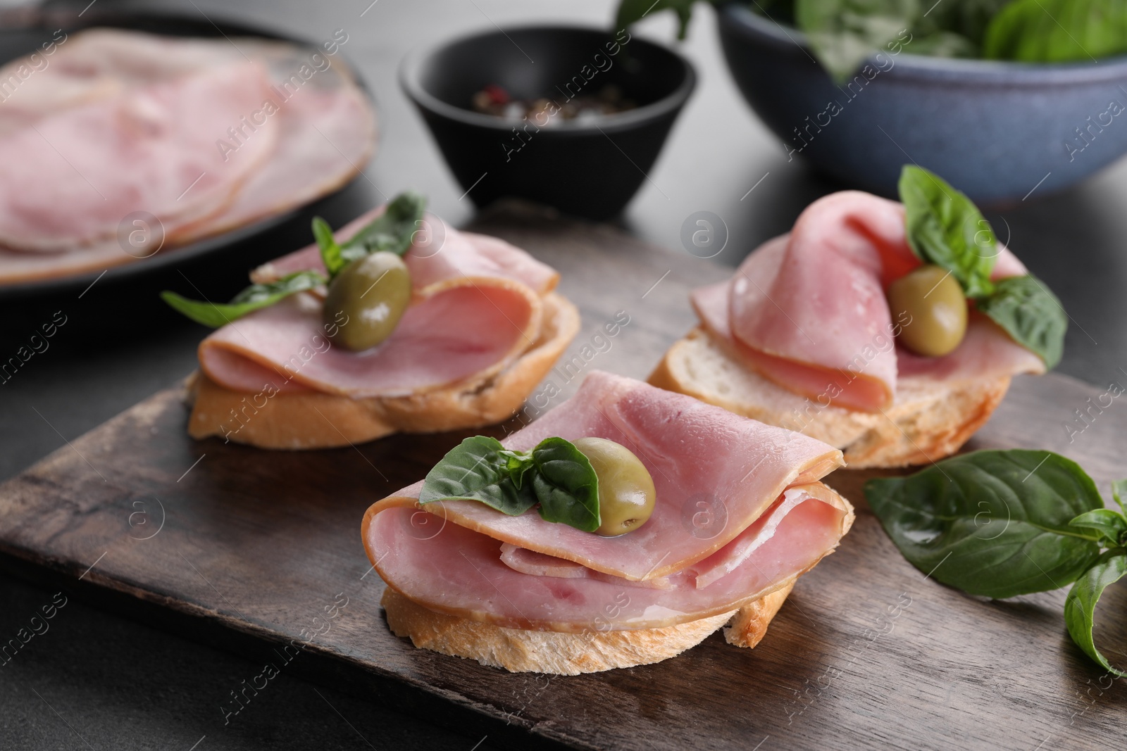 Photo of Delicious sandwiches with ham, basil and olives on table, closeup