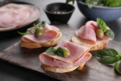 Delicious sandwiches with ham, basil and olives on table, closeup