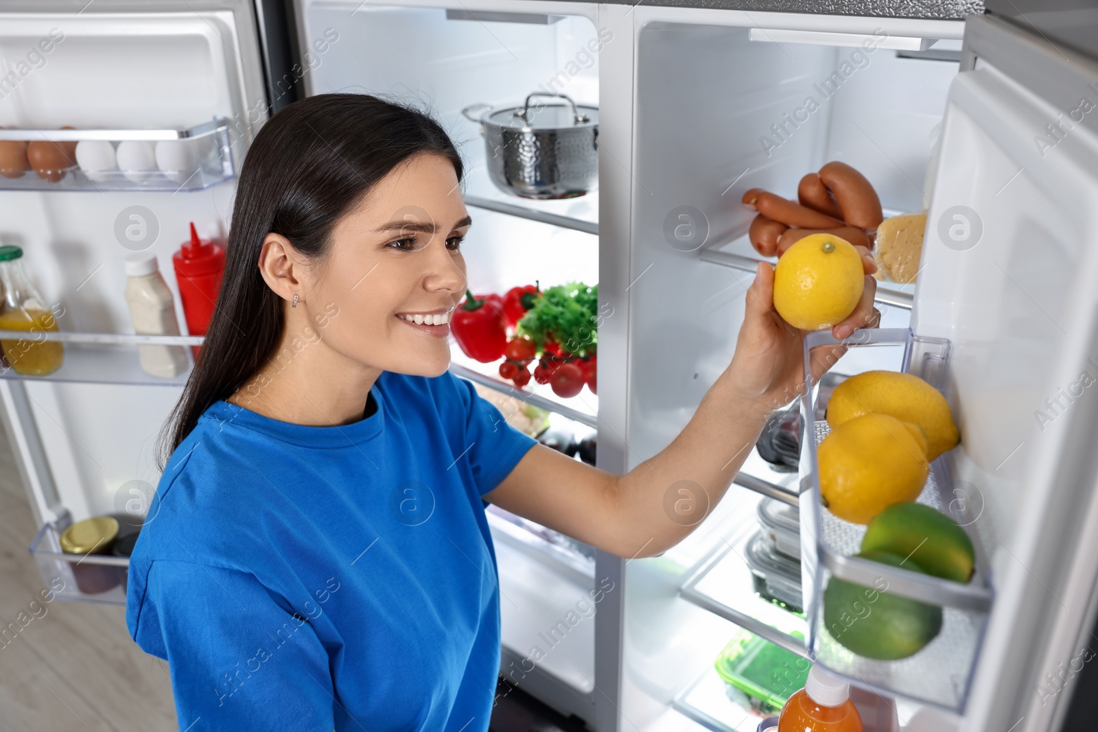 Photo of Young woman taking lemon out of refrigerator indoors
