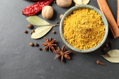 Photo of Dry curry powder in bowl and other spices on dark textured table, flat lay. Space for text