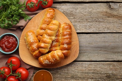 Delicious sausage rolls and ingredients on wooden table, flat lay. Space for text