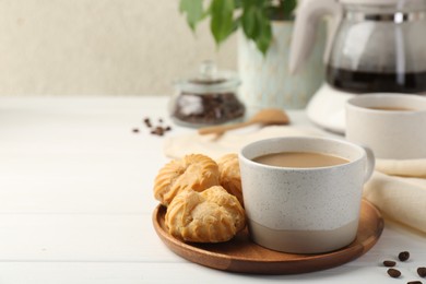 Aromatic coffee in cup and tasty profiteroles on white wooden table, space for text