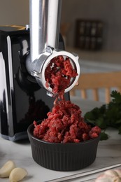 Electric meat grinder with beef mince and products on white marble table in kitchen