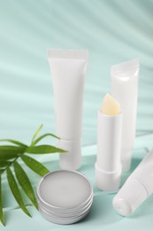 Photo of Different lip balms and palm leaf on light blue background