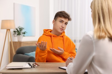 Psychologist working with teenage boy at table in office