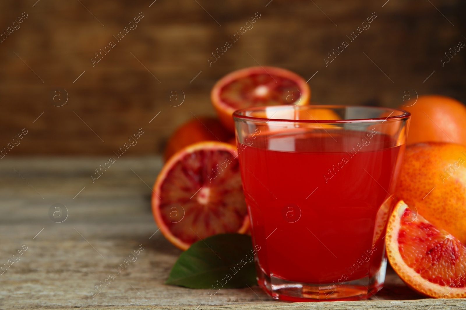 Photo of Tasty sicilian orange juice in glass and fruits on wooden table. Space for text