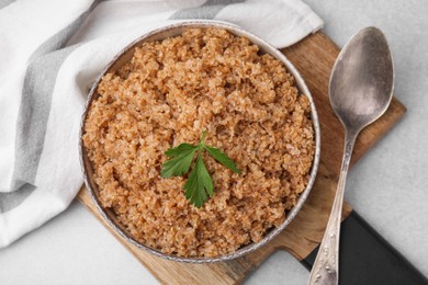 Photo of Tasty wheat porridge with parsley in bowl and spoon on white tiled table, top view