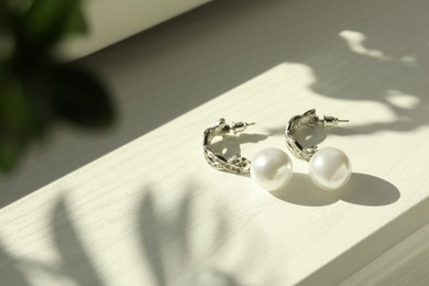 Elegant silver earrings with pearls on white wooden table, closeup view. Space for text