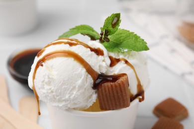 Photo of Scoops of tasty ice cream with caramel sauce, mint leaves and candies on table, closeup