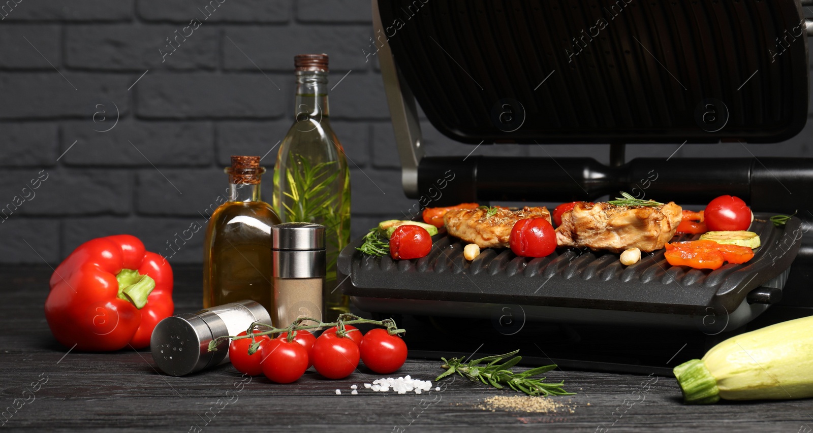 Photo of Electric grill with different products on black wooden table