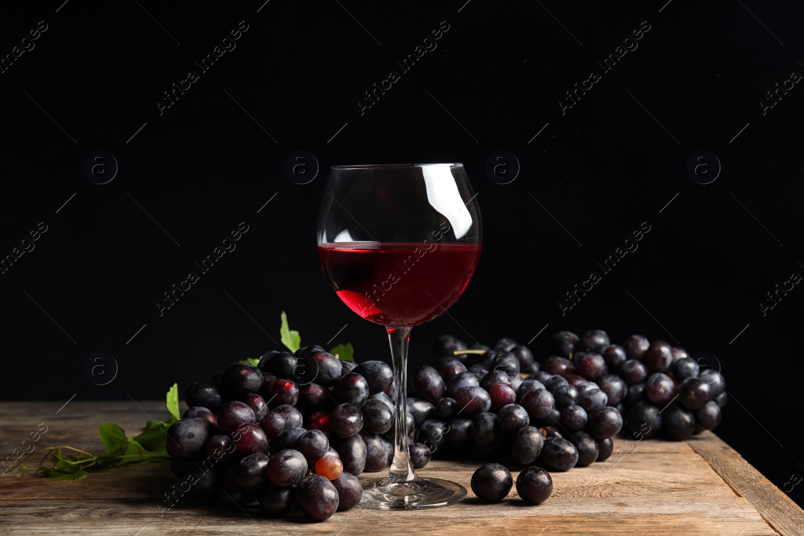 Photo of Fresh ripe juicy grapes and glass of red wine on table against black background