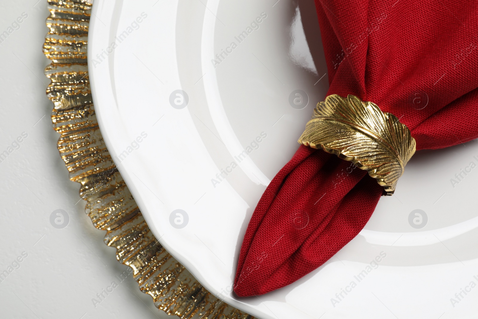 Photo of Red fabric napkin and decorative ring for table setting on white plate, top view