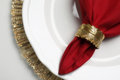 Red fabric napkin and decorative ring for table setting on white plate, top view