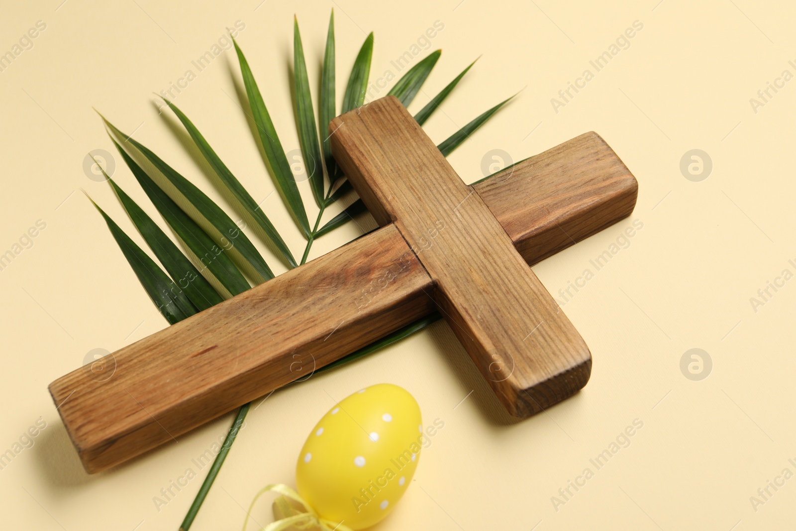 Photo of Wooden cross, painted Easter egg and palm leaf on beige background