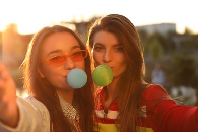 Photo of Beautiful young women blowing bubble gums and taking selfie outdoors