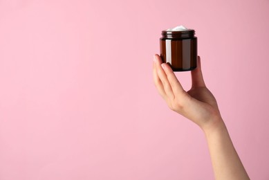 Photo of Woman with jar of face cream on pale pink background, closeup. Space for text