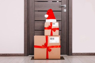 Photo of Christmas gift boxes and Santa hat near door indoors. Sending present by mail