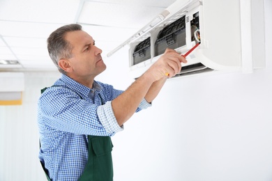 Photo of Electrician with screwdriver repairing air conditioner indoors