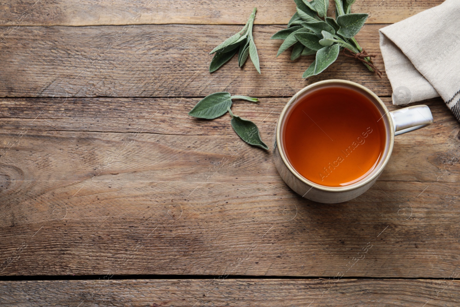 Photo of Cup of aromatic sage tea and fresh leaves on wooden table, above view. Space for text