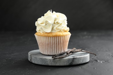 Photo of Tasty cupcake with cream and vanilla pods on black table, closeup