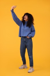 Beautiful young woman taking selfie with smartphone on orange background