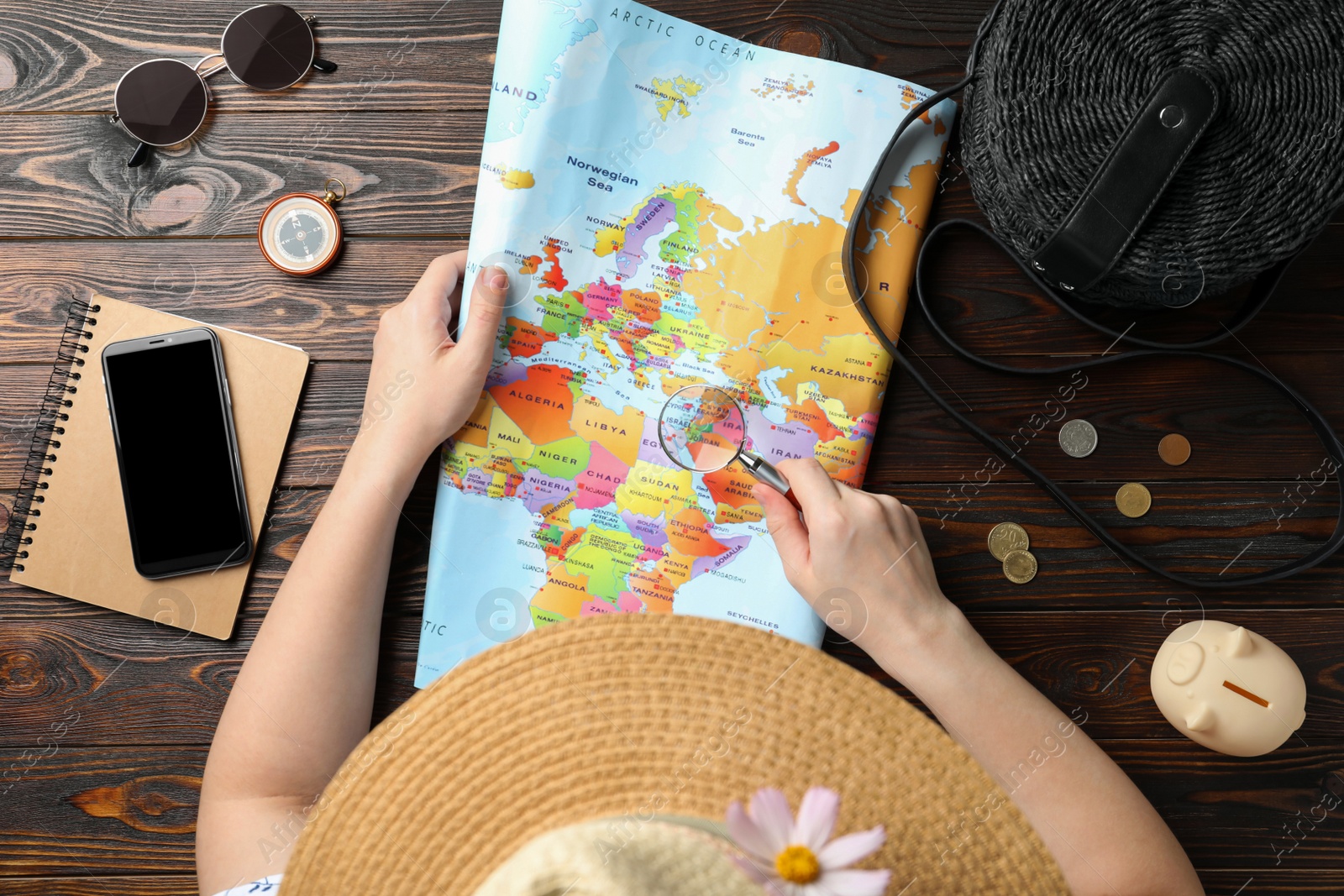 Photo of Woman looking through magnifying glass on world map at wooden table, closeup. Travel during summer vacation