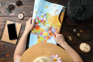 Photo of Woman looking through magnifying glass on world map at wooden table, closeup. Travel during summer vacation