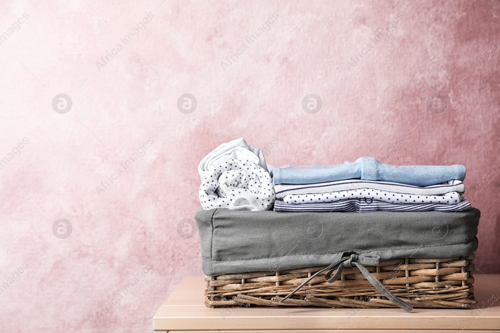 Photo of Basket with baby clothes on table near color wall. Space for text