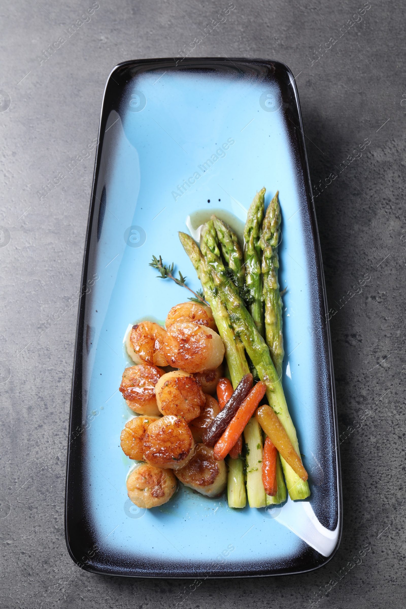 Photo of Delicious fried scallops with asparagus and vegetables on grey table, top view