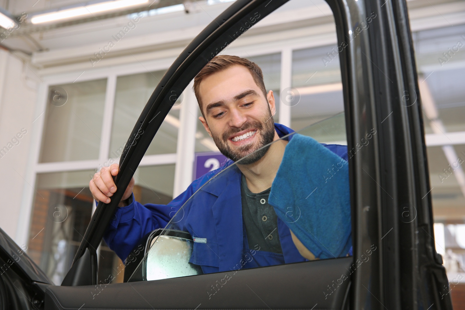 Photo of Worker cleaning automobile window glass with rag at car wash