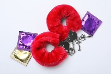 Furry handcuffs and condoms on white background, top view. Sex game