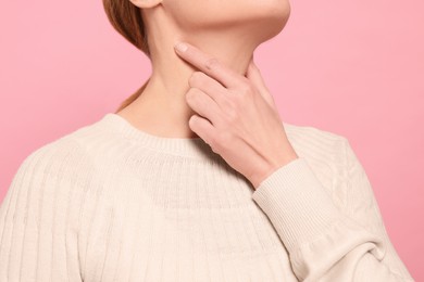 Woman suffering from sore throat on pink background, closeup