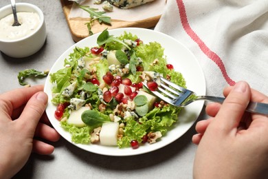 Photo of Woman eating fresh salad with pear at grey table, closeup