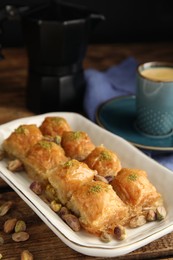 Delicious baklava with pistachios, hot drink and scattered nuts on wooden table, closeup