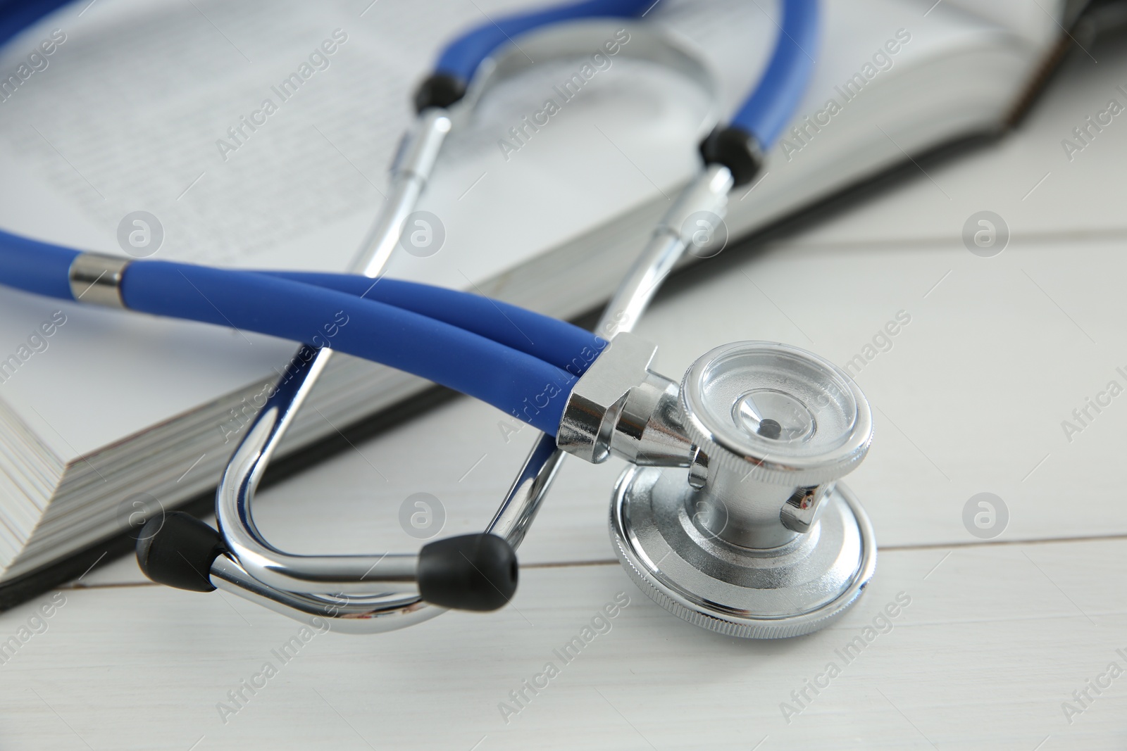 Photo of One medical stethoscope and book on white wooden table, closeup