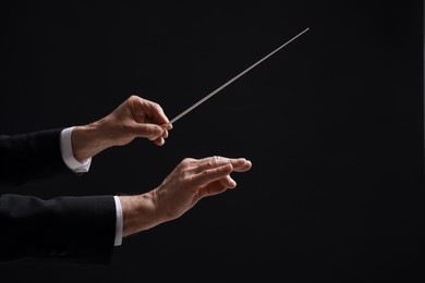 Photo of Professional conductor with baton on black background, closeup