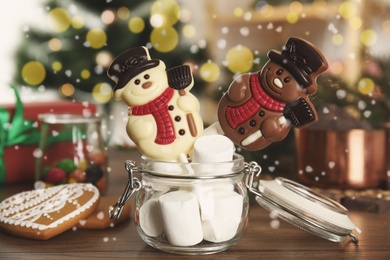 Funny chocolate snowmen candies in glass jar full of marshmallows on wooden table, closeup