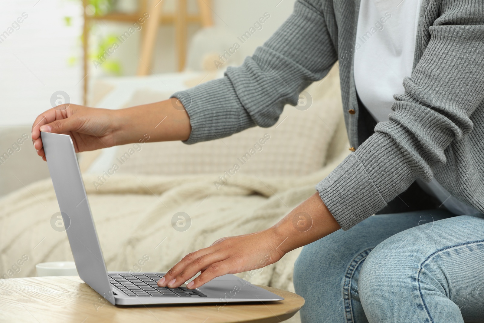 Photo of Woman using laptop at wooden coffee table indoors, closeup