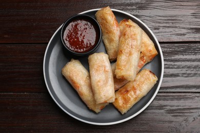 Photo of Tasty fried spring rolls and sauce on wooden table, top view