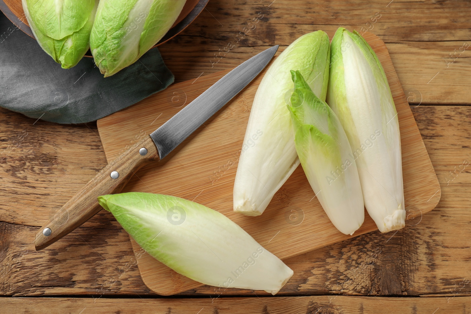 Photo of Fresh raw Belgian endives (chicory), board and knife on wooden table, top view