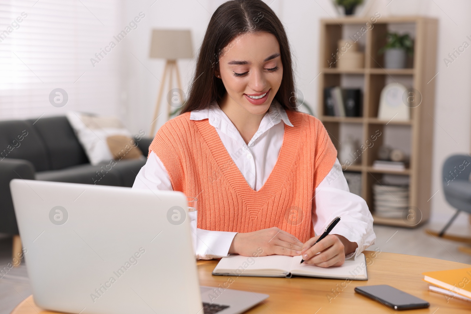 Photo of Young woman writing in notebook at wooden table indoors