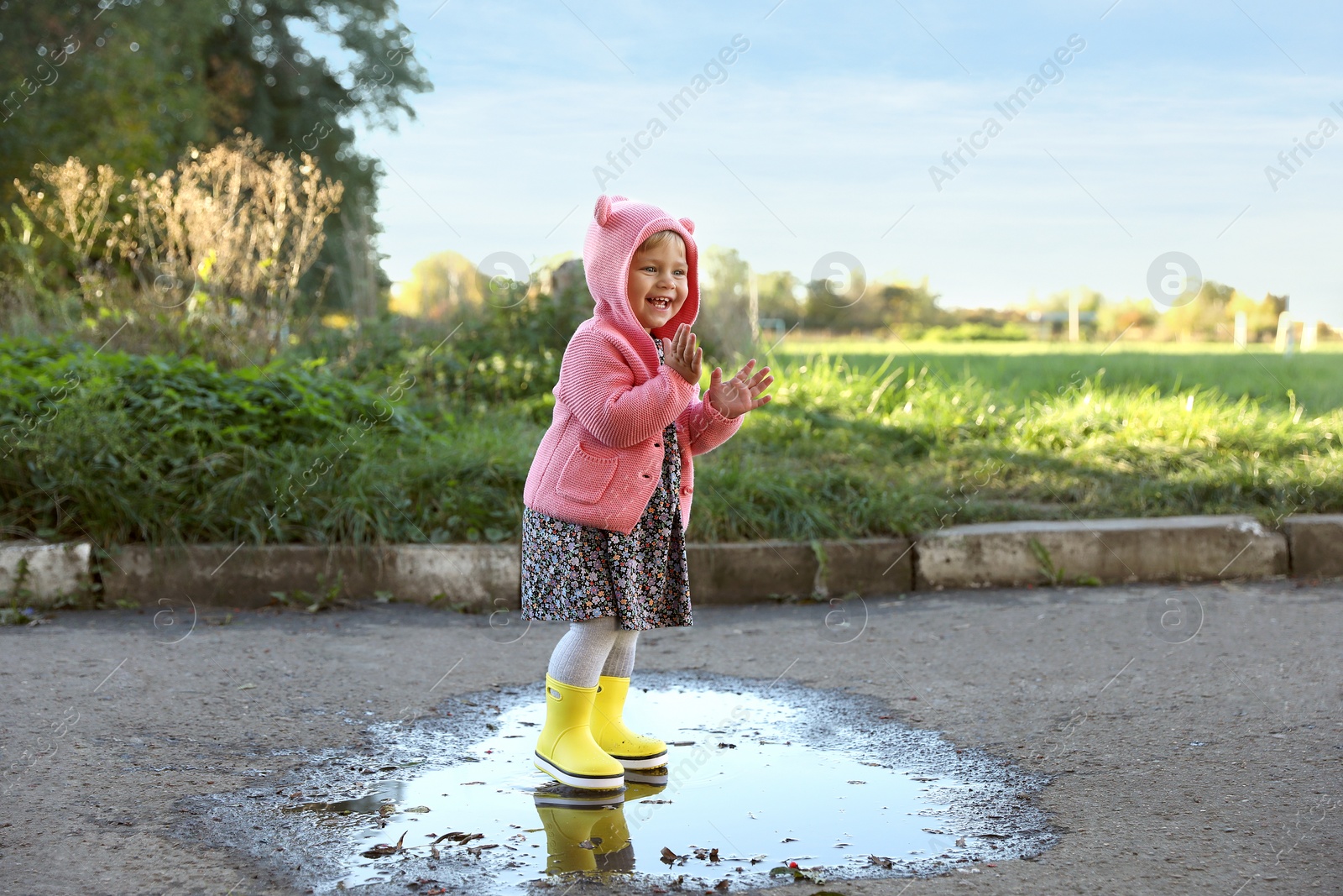 Photo of Little girl wearing rubber boots standing in puddle outdoors. Autumn walk