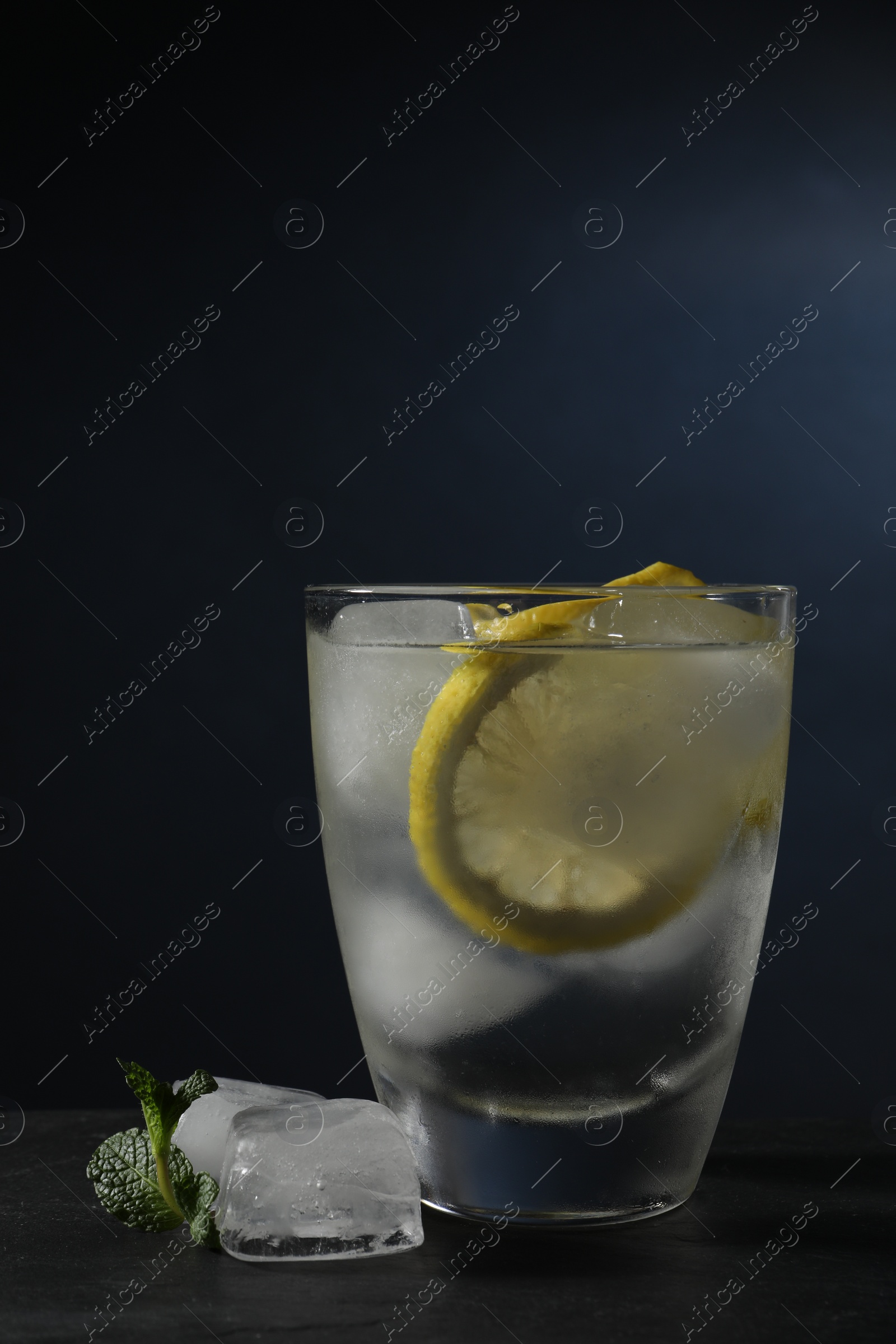 Photo of Shot of vodka with lemon, ice and mint on black table
