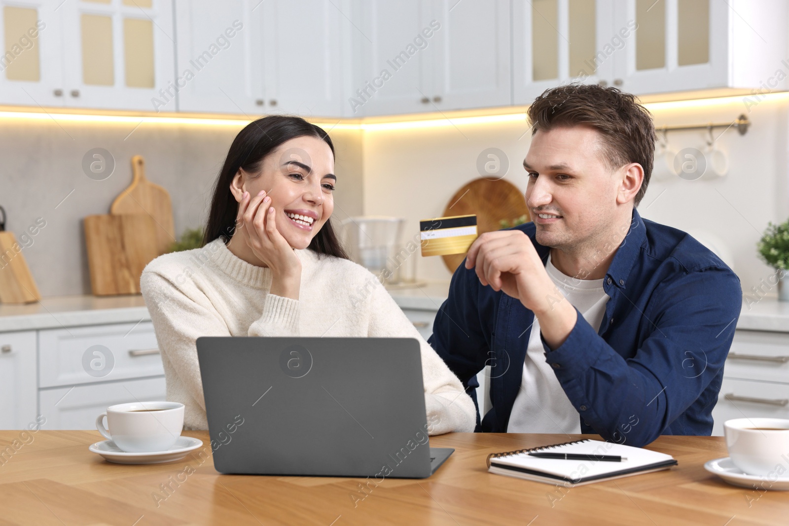 Photo of Happy couple with laptop and credit card shopping online at wooden table in kitchen
