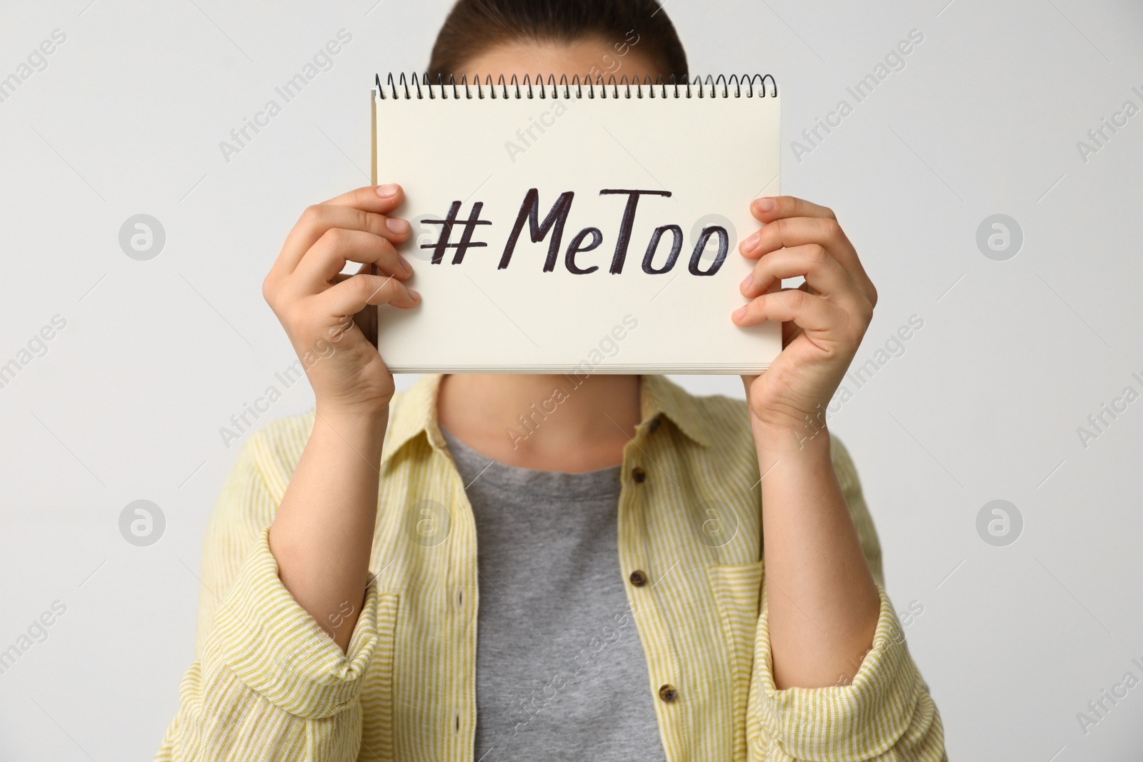 Photo of Woman holding notebook with hashtag MeToo against light background, closeup. Stop sexual assault