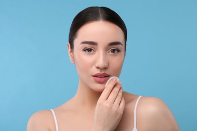 Photo of Beautiful woman removing makeup with cotton pad on light blue background