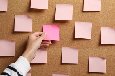 Photo of Woman taking empty paper note from cork board, closeup